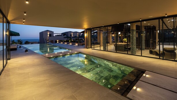 A modern outdoor pool area with glass walls, a clear view of the ocean, and a well-lit patio. - Tetra Retreat (Kefalonia)