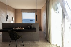 Un interior moderno con vista al mar, un escritorio de tonos oscuros, una silla y un ventanal con cortinas.