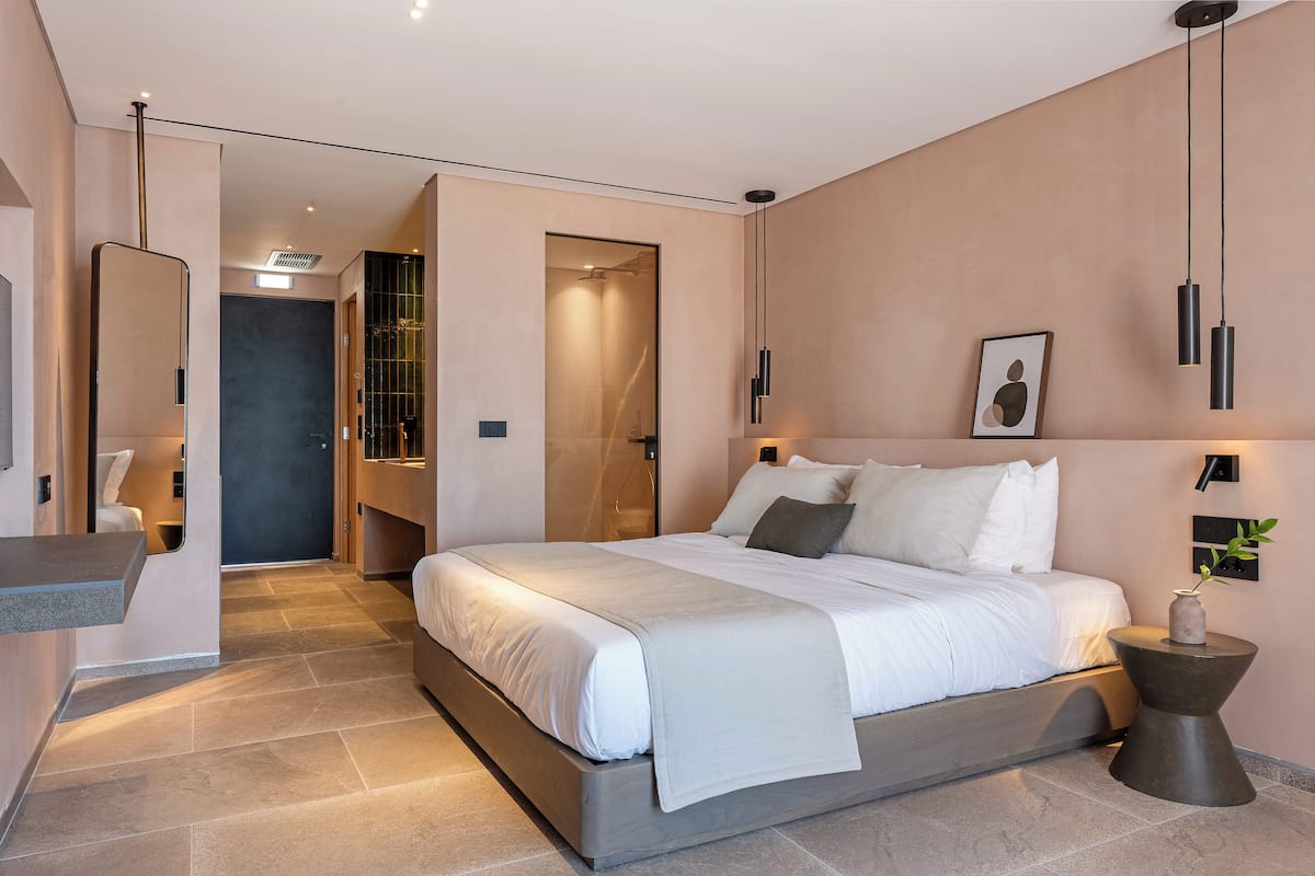 A modern bedroom with a large bed, bedside tables, a mirror, and a shower area.
