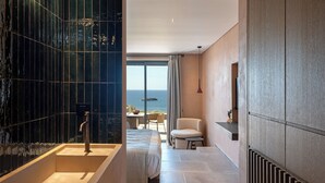 A modern hotel room with a large bathtub, a bed, a seating area with a view of the sea, and a large window. - Tetra Retreat (Kefalonia)