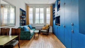 Et værelse med spisebord, stole, sofa, en lænestol og en reol.