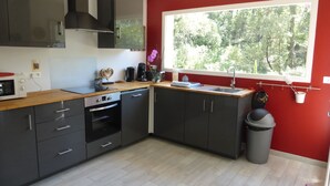 Una cucina moderna con mobili grigi, un piano di lavoro in legno, forno integrato e una finestra vista alberi.