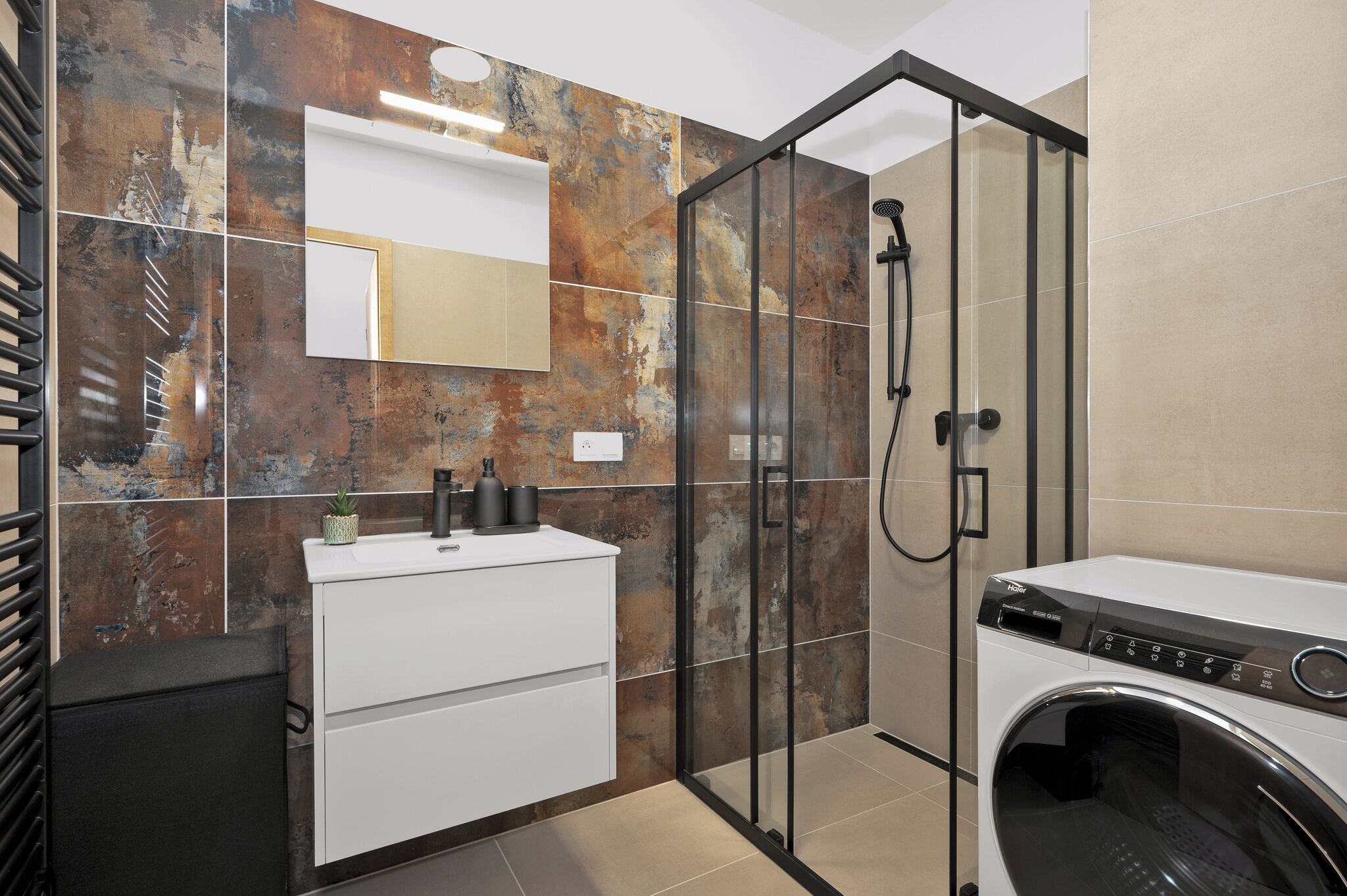Een moderne badkamer met een douchecabine van glas, een inbouw wastafel en een voorlader wasmachine.
