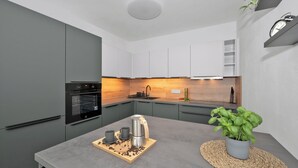 A modern kitchen with grey cabinets, a built-in oven, a coffee machine, and a potted basil plant. - Fully equipped apartments with Terraces, Free garage parking, Netflix & AC - by Apartmány Šlapanice cz (Slapanice)