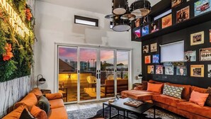 A modern living room with a large window, orange sofas, a black coffee table, and a wall decorated with framed pictures.