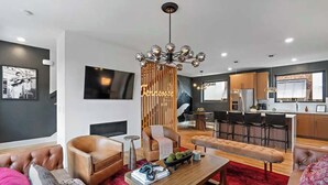 A modern living room with a leather sofa, a wooden coffee table, and a red rug. There is a kitchen area with a bar and a dining table.