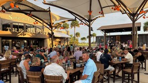 An outdoor dining area with wooden tables and chairs, a large awning, and a building with a sign reading "Sawgrass Grove The Market". - 5 O`Clock Somewhere - 3/2 w/ Golf Cart in The Village of Lake Denham (The Villages)