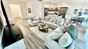 A modern living room with a sectional sofa, a coffee table, and a TV stand. - 5 O`Clock Somewhere - 3/2 w/ Golf Cart in The Village of Lake Denham (The Villages)