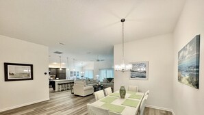A spacious living area with a dining table, chairs, and a chandelier. There is a kitchen in the background with a bar and a seating area with a sofa and chairs. - 5 O`Clock Somewhere - 3/2 w/ Golf Cart in The Village of Lake Denham (The Villages)
