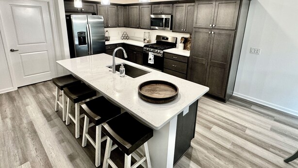 A modern kitchen with dark cabinets, a large island with bar stools, stainless steel appliances, and pendant lighting. - 5 O`Clock Somewhere - 3/2 w/ Golf Cart in The Village of Lake Denham (The Villages)