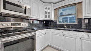 Una cucina moderna con mobili bianchi, piano cottura in acciaio inossidabile, forno a microonde e una finestra con vista.