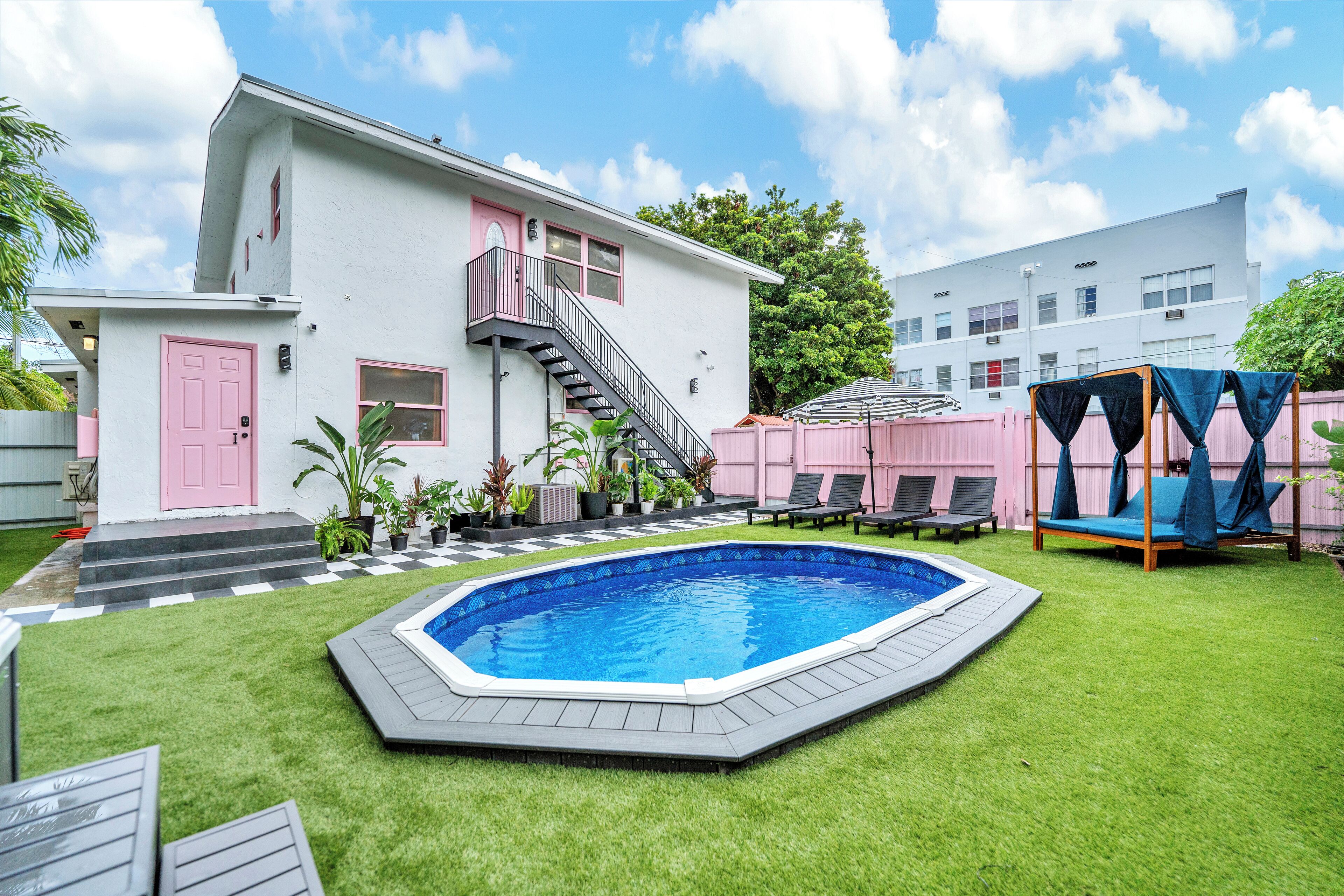 Un patio con piscina, una escalera que lleva a un balcón y un edificio con una puerta rosa.