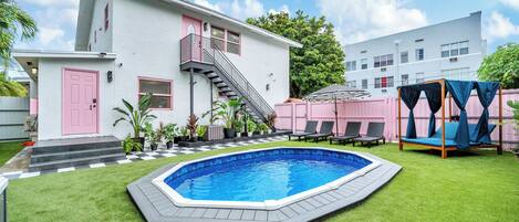 Un patio con piscina, una escalera que lleva a un balcón y un edificio con una puerta rosa.