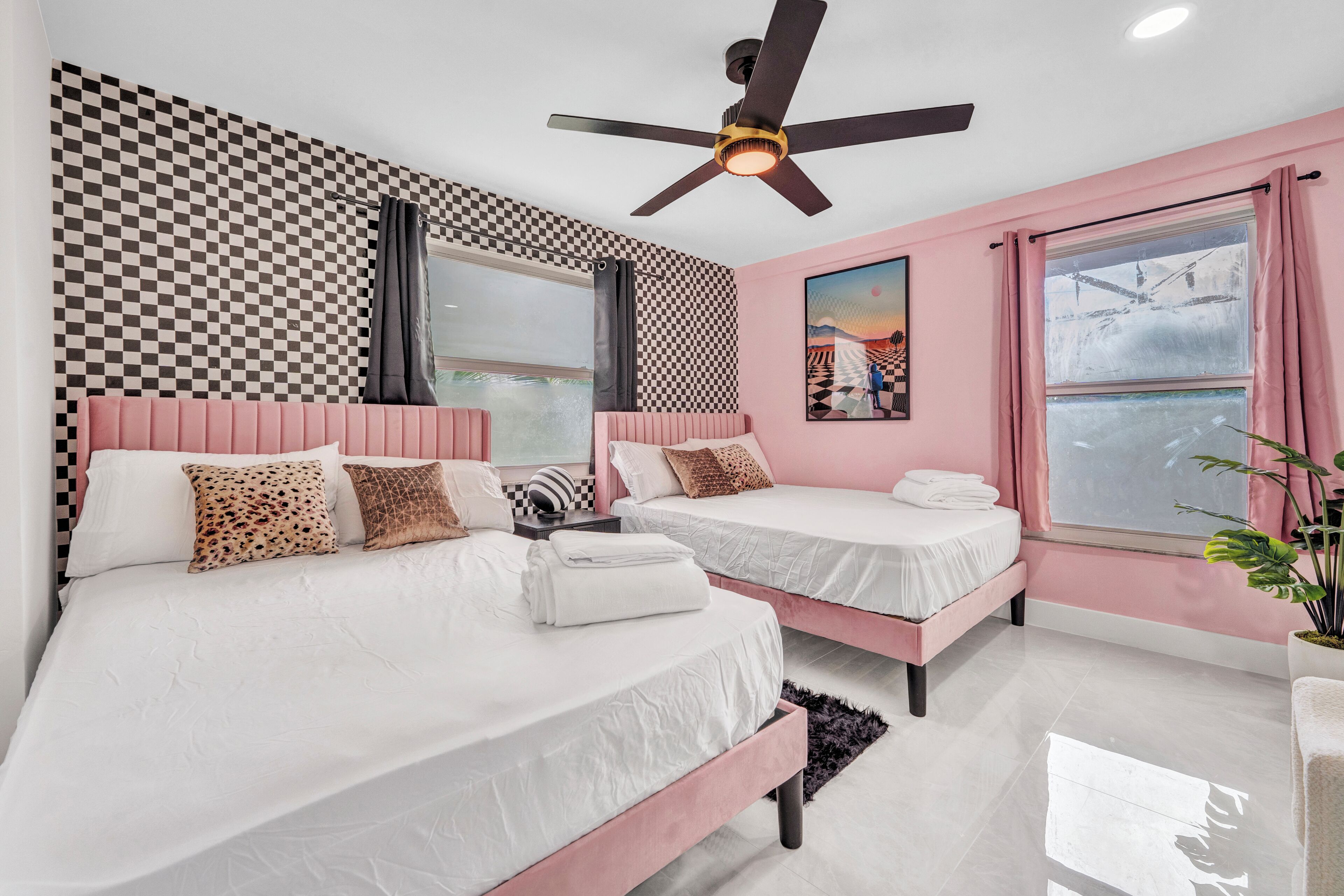 A bedroom with two beds, a ceiling fan, and a large window with pink curtains.