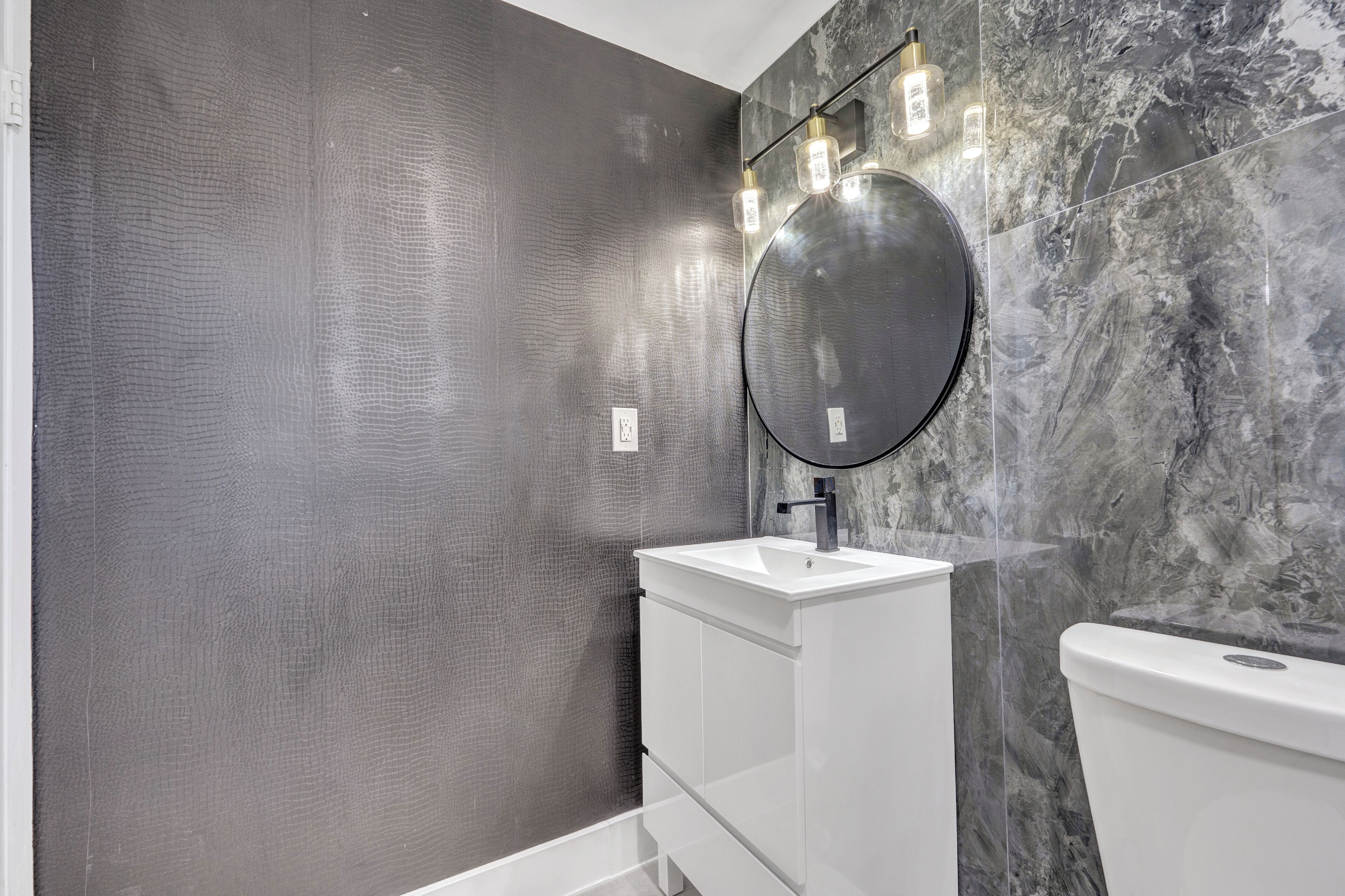 A bathroom with a white vanity, a round mirror, and a toilet.