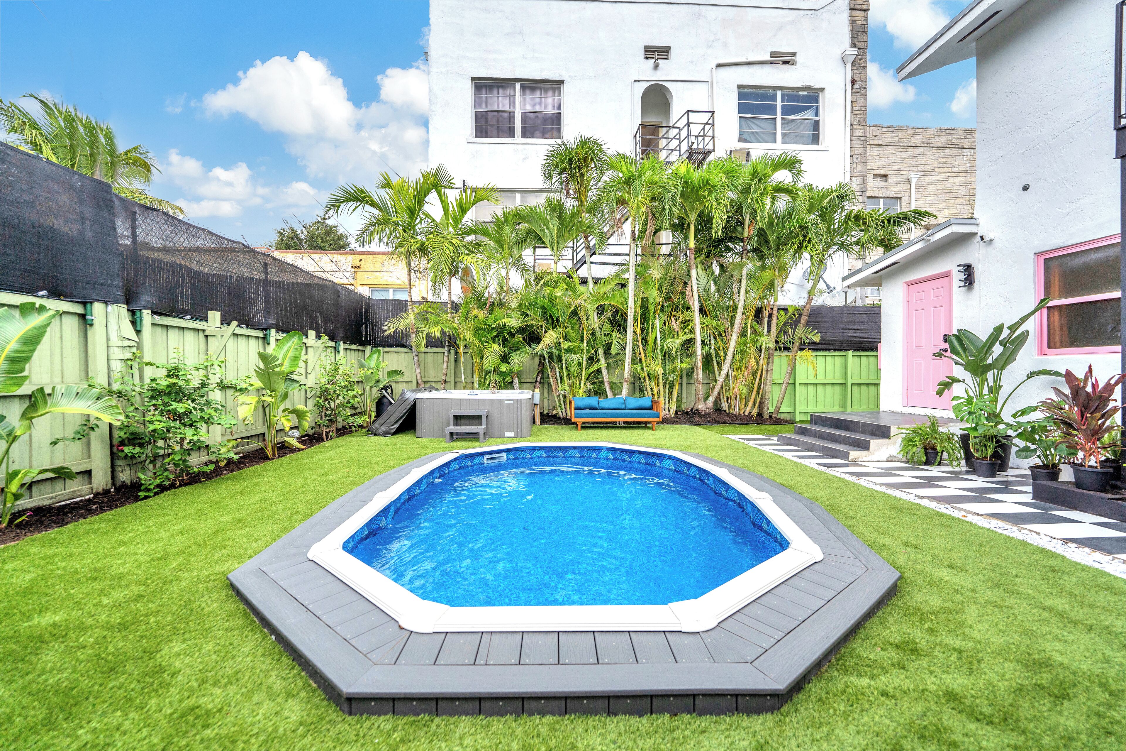 A backyard with a swimming pool, green lawn, and a wooden fence.