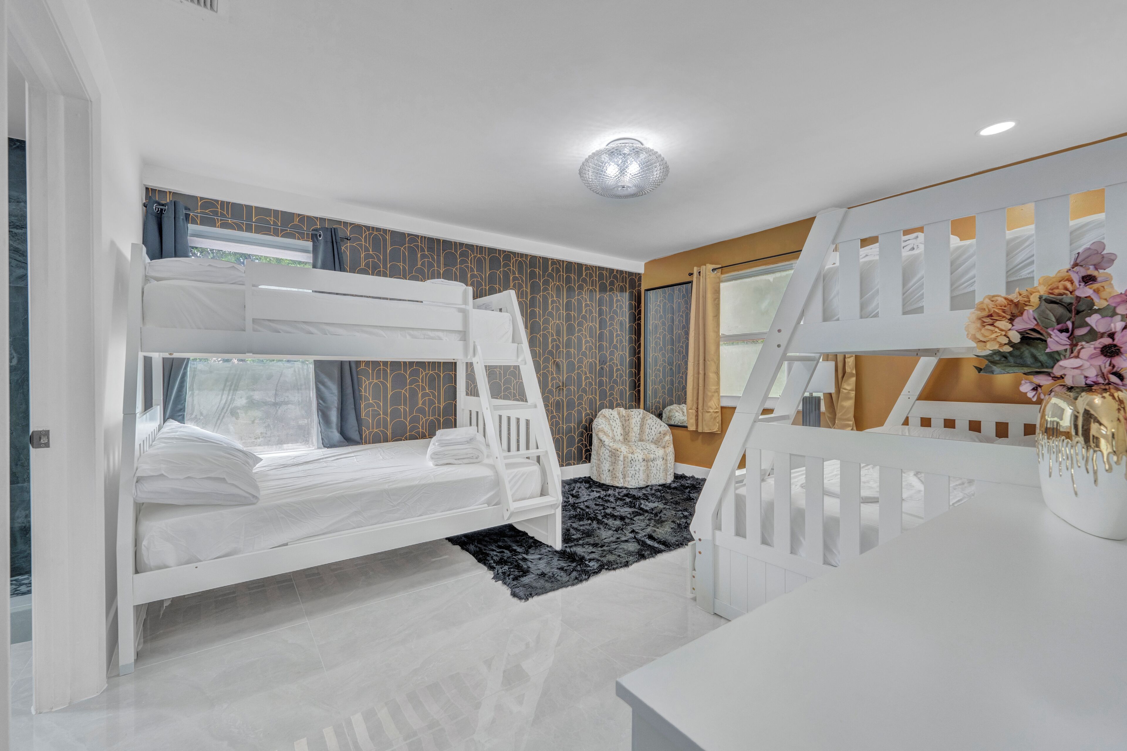 Dormitorio con literas, un escritorio blanco, una silla y un jarrón decorativo.