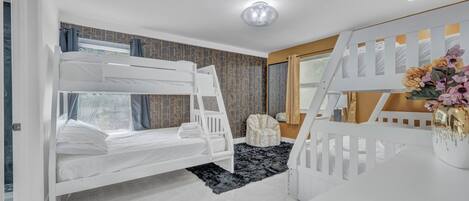 Dormitorio con literas, un escritorio blanco, una silla y un jarrón decorativo.
