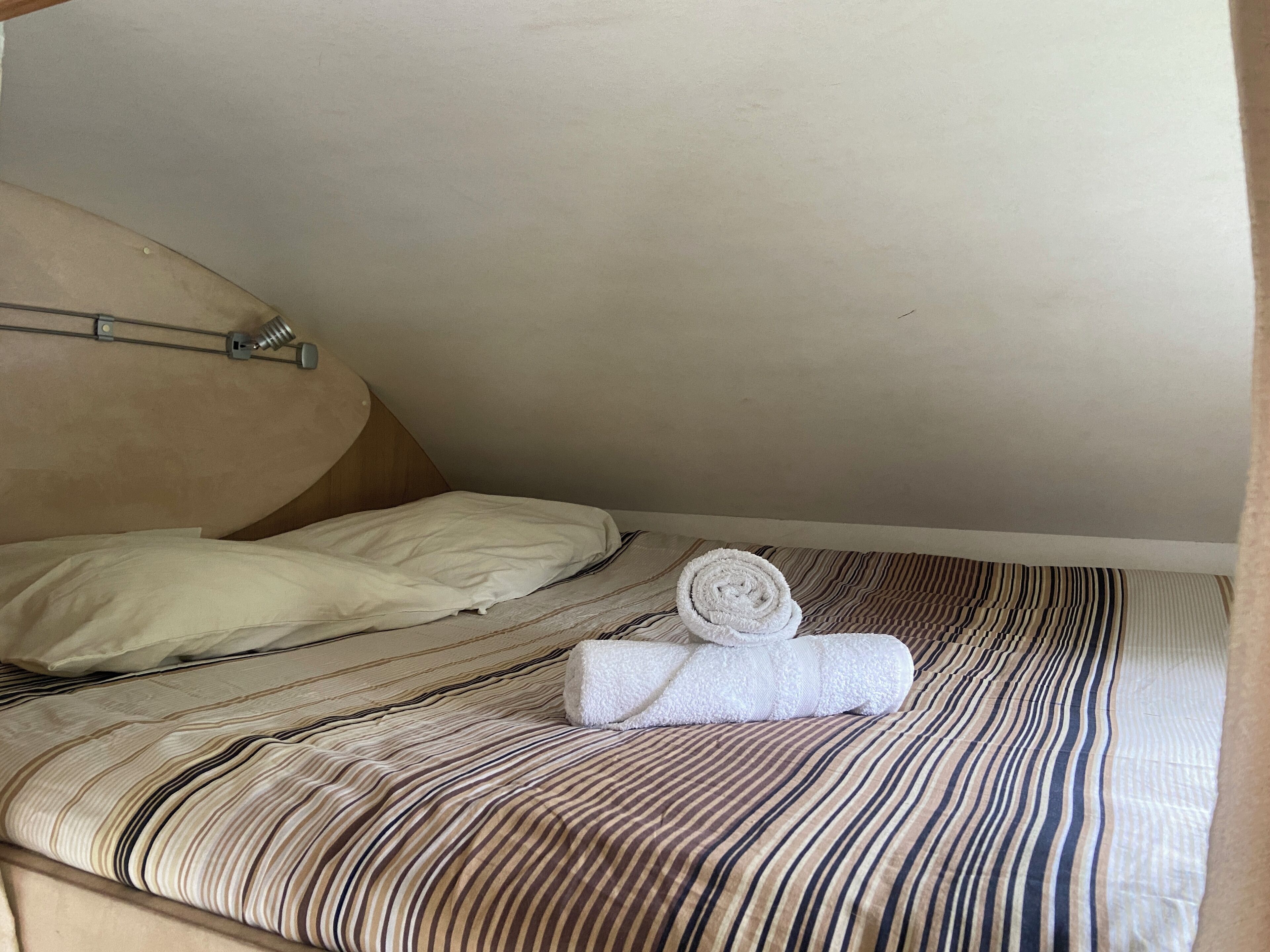 Un lit simple avec une couvre-lit à rayures, une serviette blanche enroulée et une tête de lit.