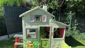 Una casetta dei giochi per bambini con angolo cucina, tavolo da pranzo e un piccolo giardino.