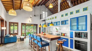 A modern kitchen with blue cabinets, a wooden island with bar stools, and hanging pendant lights. - Holiday Villa 3BR Sea View An Bang Beach (Da Nang)