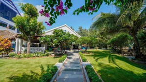 A well-maintained garden with a pathway leading to a white building, surrounded by lush greenery and palm trees. - Holiday Villa 3BR Sea View An Bang Beach (Da Nang)