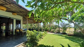 An outdoor seating area with a thatched roof, surrounded by lush greenery and a well-maintained lawn. - Holiday Villa 3BR Sea View An Bang Beach (Da Nang)