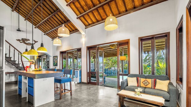 A spacious living area with a wooden ceiling, a sofa with cushions, a coffee table, and a kitchen area with a bar stool. - Holiday Villa 3BR Sea View An Bang Beach (Da Nang)