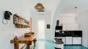 Μια κουζίνα με λευκά ντουλάπια, ένα ξύλινο τραπέζι και ένα φωτιστικό που κρέμεται από την οροφή.