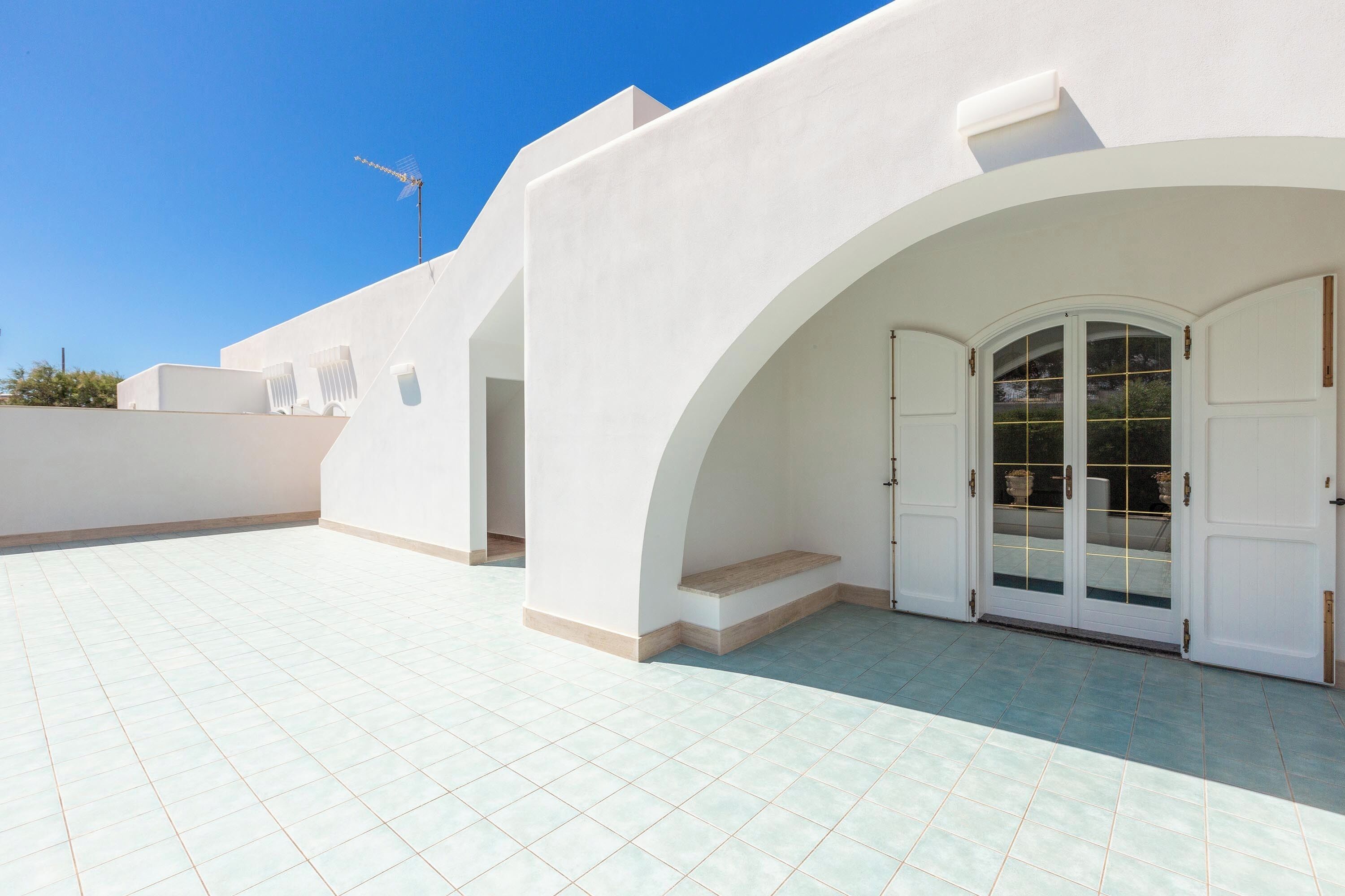 Um edifício moderno com fachada branca, uma entrada em arco grande e um espaço de pátio com azulejos.