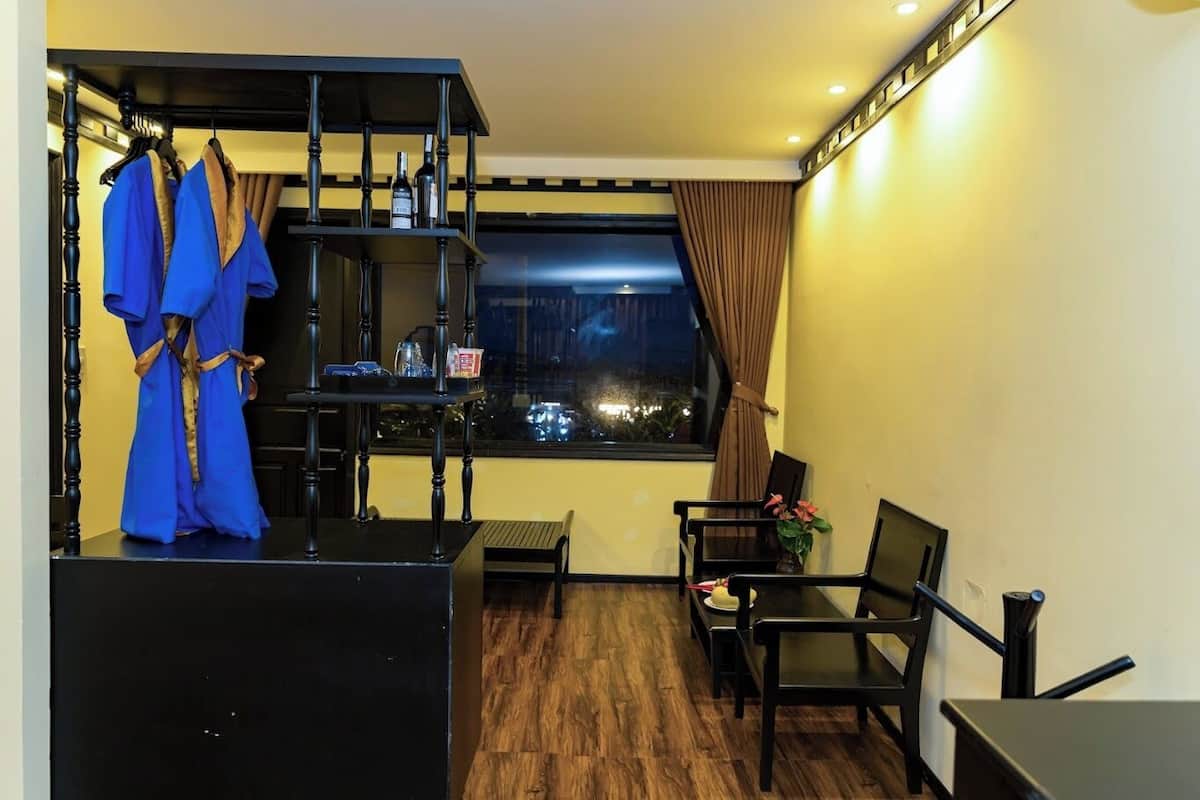 A room with a black desk, a chair, a small table, a window with curtains, and a blue robe hanging on a rack.