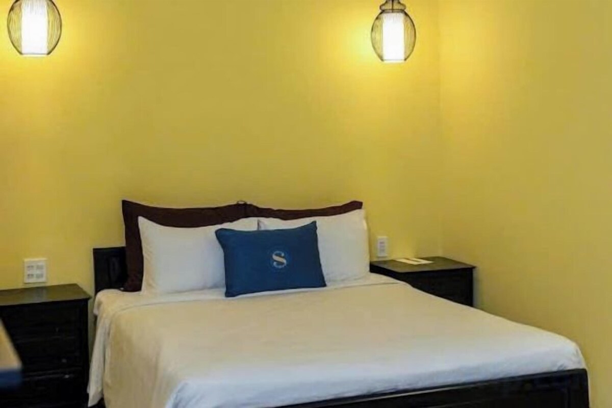 Una cama individual con cabecera de madera, dos lámparas de noche y una almohada azul.