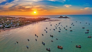 A coastal scene with boats on the water and a sunset in the background. - Sabina Boutique Hotel & Villa Mui Ne (Mui Ne)