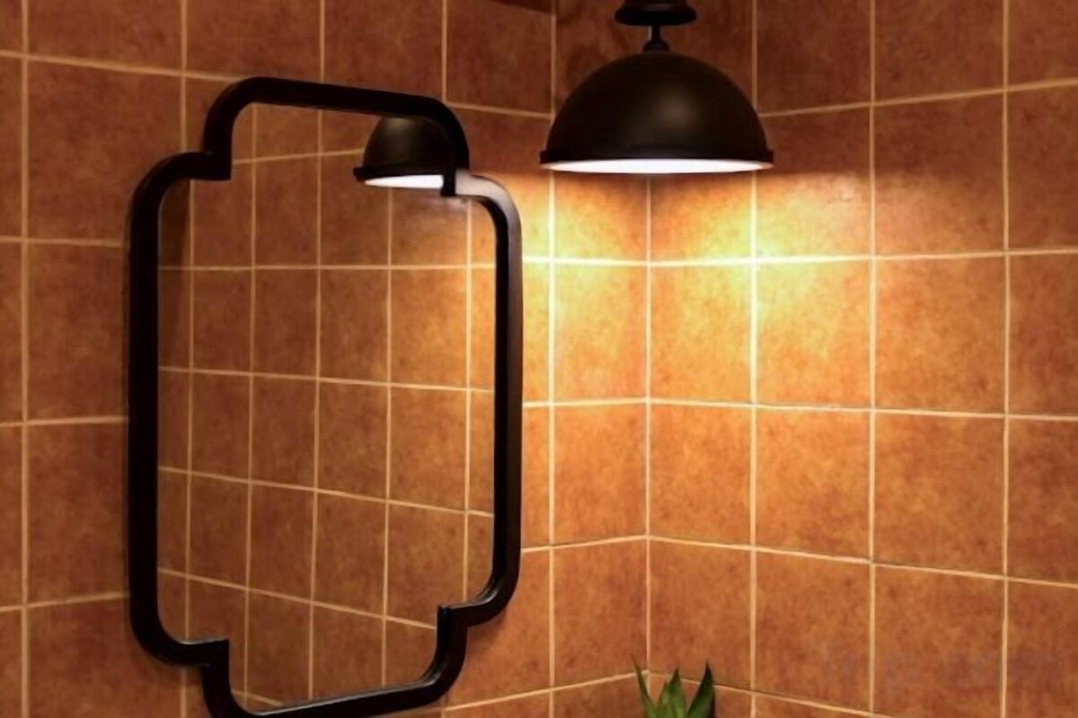 A wall-mounted mirror with a black frame and a single light fixture above it.