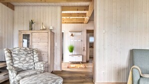 Una habitación acogedora con techo de madera, un sofá estampado con hojas, un armario y una pequeña mesa con una planta.