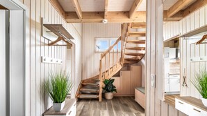 Un interior de madera con una escalera, paredes blancas y plantas en macetas.