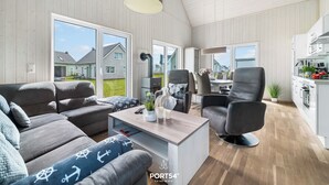 Ein modernes Wohnzimmer mit einer Couch, Sesseln, einem Couchtisch und einer Küchenzeile inklusive Schränken und Geräten.
