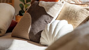 Una cama con varias almohadas y una manta, una planta en maceta y un armario de madera al fondo.