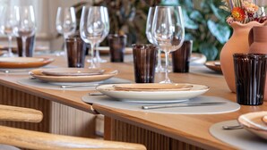 Una mesa de comedor dispuesta con platos, vasos y cubiertos, rodeada de sillas y macetas.