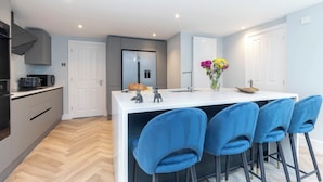 A modern kitchen with a central island, bar stools, and a decorative vase. - Elliot Oliver - Comfortable Five Bedroom Town Centre House With Garden & Garage (Cheltenham)