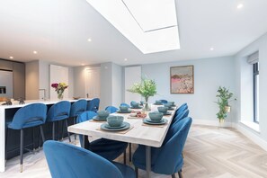 Un comedor moderno con una mesa larga dispuesta para seis comensales, sillas azules y suelo de tonos claros.