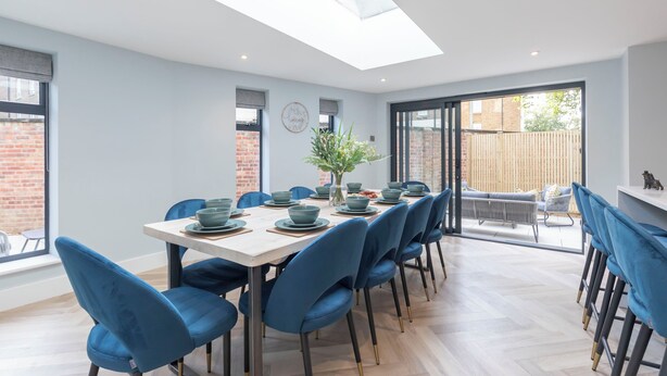 A modern dining area with a long table, blue chairs, and a skylight. - Elliot Oliver - Comfortable Five Bedroom Town Centre House With Garden & Garage (Cheltenham)