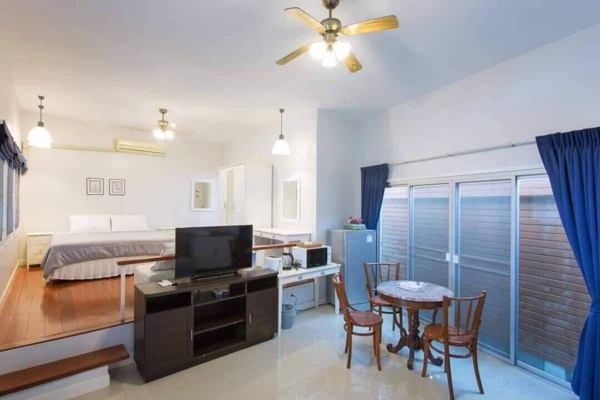 Une chambre d’hôtel moderne équipée d’un lit, d’une télévision, d’une kitchenette, d’un coin repas et d’un balcon avec des rideaux.