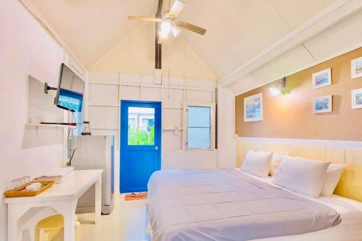 Une chambre à coucher comprenant un lit, un bureau, une télévision et une porte donnant sur un paysage verdoyant.