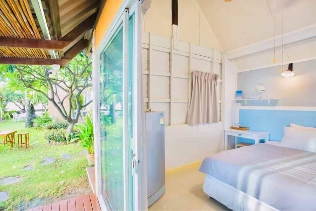 Une chambre à coucher comprenant un lit, une petite table de chevet, une commode et une fenêtre donnant sur un jardin.