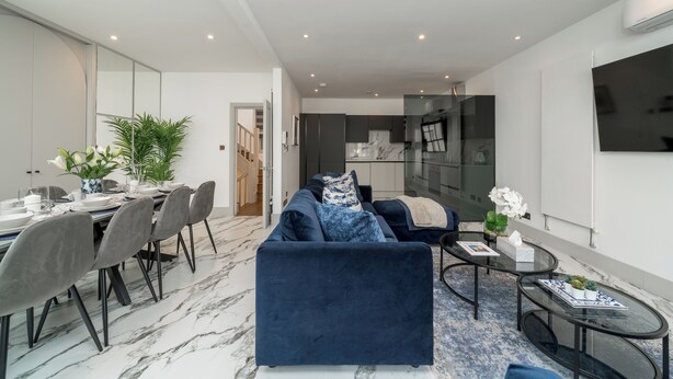 En moderne stue med en mørkeblå sofa, et glasbord og et spiseområde med marmorgulv.