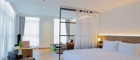A hotel room with a large bed, a desk with a laptop, a chair, and a dining area with a table and chairs.