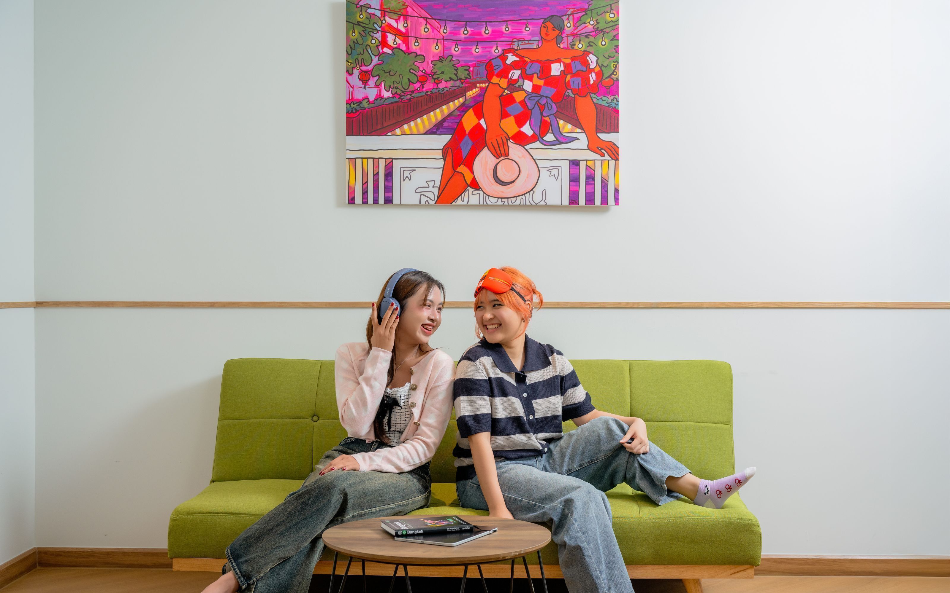 Two people sitting on a green sofa in a room with a colorful painting on the wall.