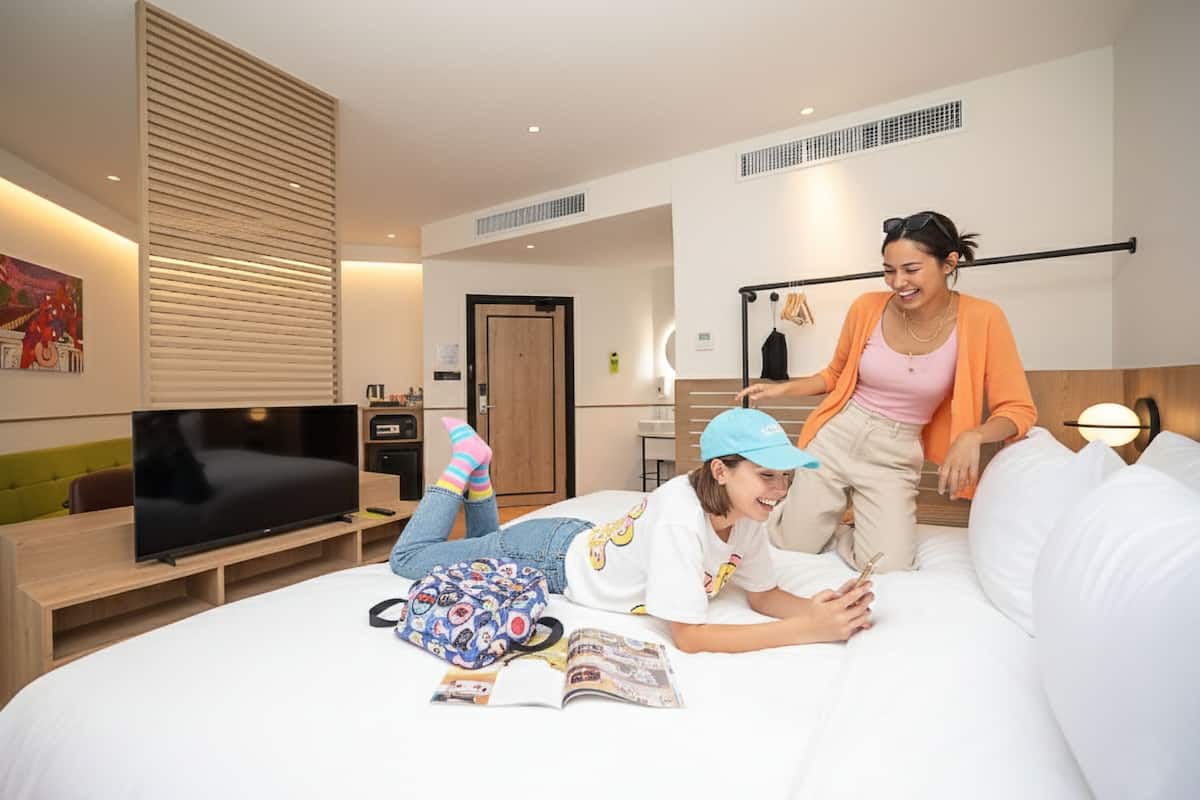 Une chambre d’hôtel moderne dotée d’un grand lit, d’une télévision, d’une petite kitchenette et d’un mur avec des lambris en bois.