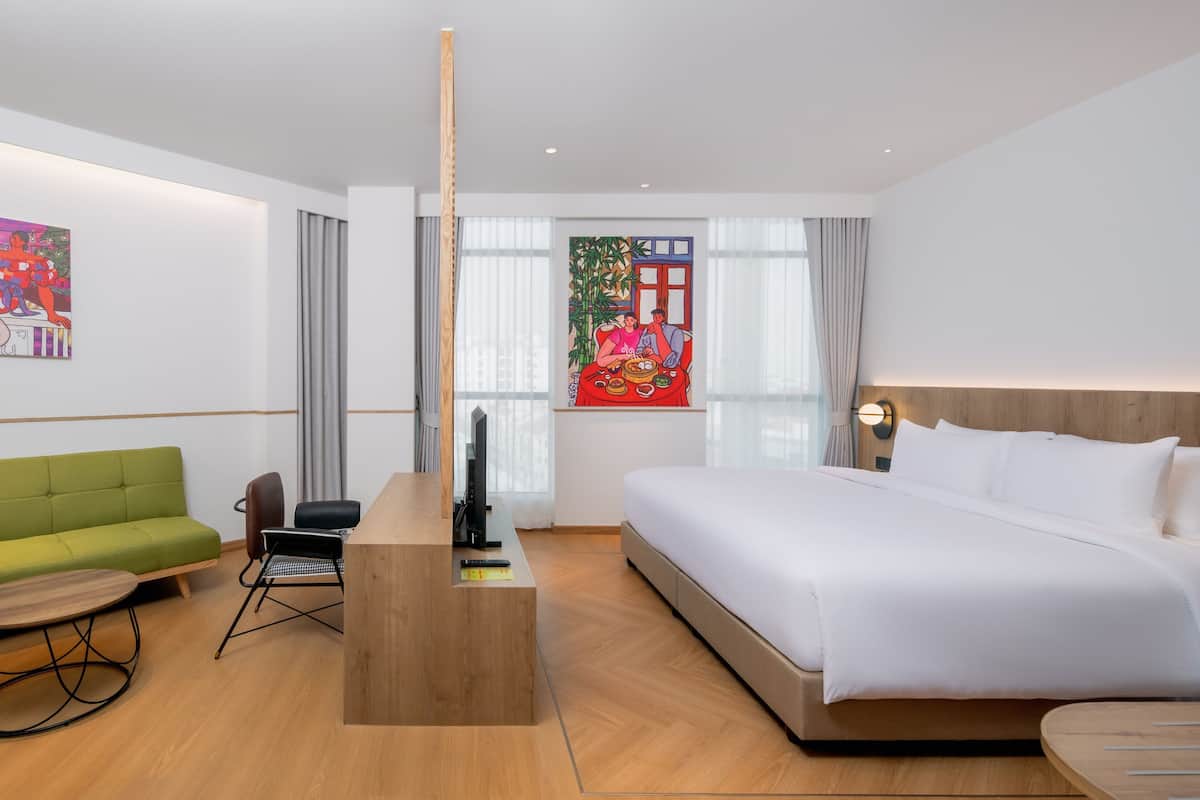 Une chambre d’hôtel avec un lit, un bureau, un canapé vert et un tableau au mur.